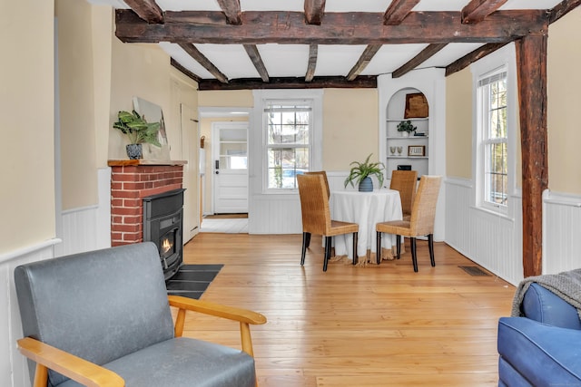 dining area with light hardwood / wood-style floors, a wood stove, built in shelves, radiator, and beamed ceiling