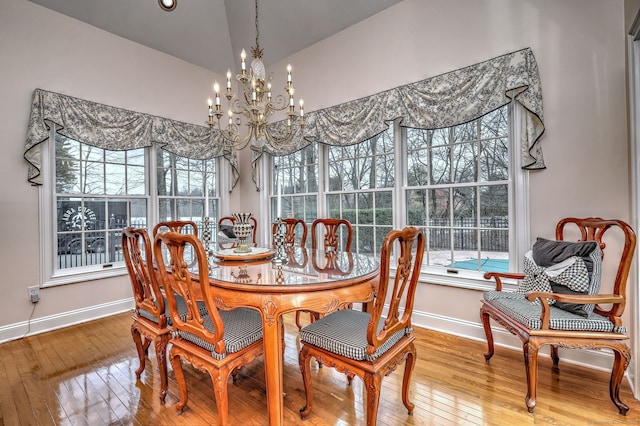 dining space with wood-type flooring, vaulted ceiling, and an inviting chandelier