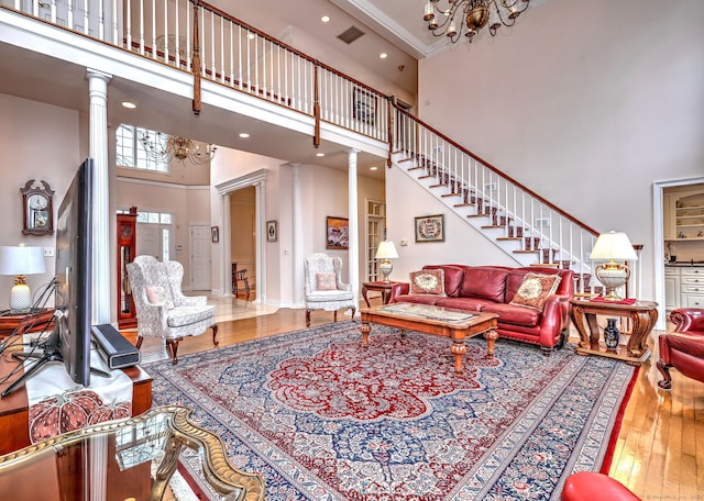 living room with hardwood / wood-style floors, a notable chandelier, a high ceiling, and ornate columns