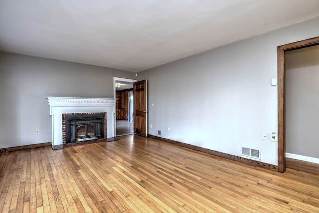 unfurnished living room with light wood-type flooring and a brick fireplace