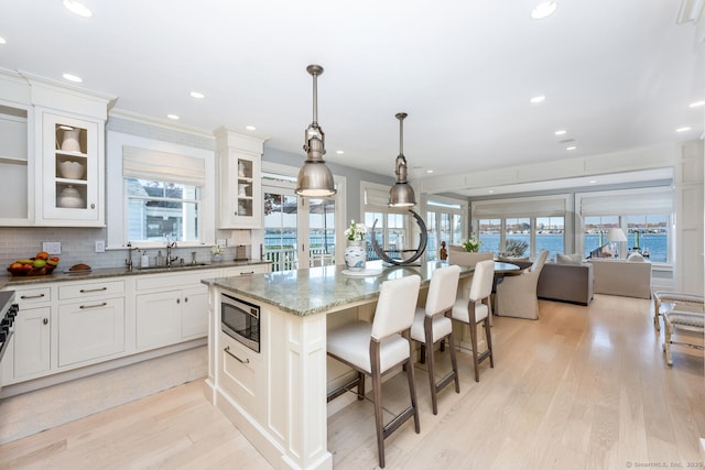 kitchen with light stone countertops, light wood-style flooring, a sink, stainless steel microwave, and a kitchen breakfast bar