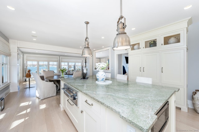 kitchen with light stone counters, light wood-style flooring, pendant lighting, and a warming drawer