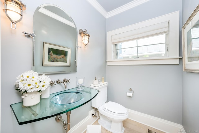 bathroom with crown molding, toilet, baseboards, and a sink