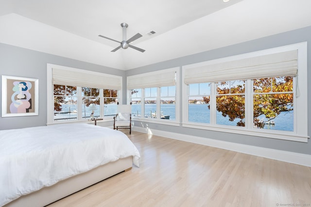 bedroom featuring visible vents, baseboards, a water view, wood finished floors, and a ceiling fan