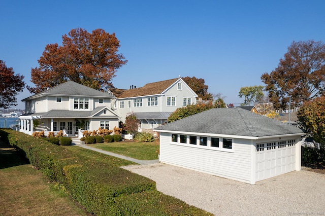 shingle-style home featuring a front yard, covered porch, a shingled roof, an outdoor structure, and a detached garage