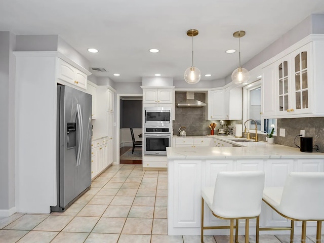 kitchen with appliances with stainless steel finishes, wall chimney exhaust hood, decorative light fixtures, sink, and kitchen peninsula