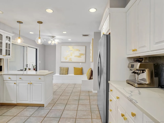 kitchen featuring ceiling fan, light tile patterned flooring, light stone countertops, white cabinets, and stainless steel fridge