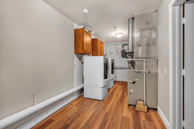 laundry room with washing machine and clothes dryer, light wood-type flooring, and cabinets