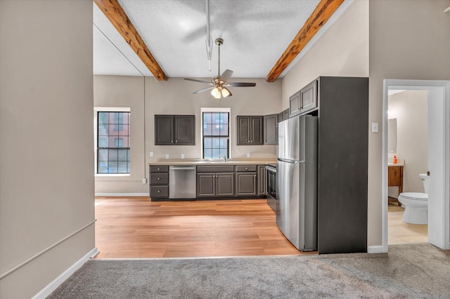 kitchen featuring stainless steel appliances, light colored carpet, gray cabinets, and beamed ceiling