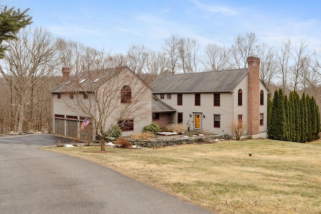 view of front facade with a garage, driveway, a front lawn, and a chimney