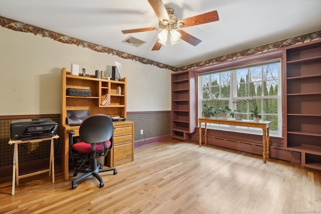 office space featuring light wood-style flooring, visible vents, a wainscoted wall, and ceiling fan