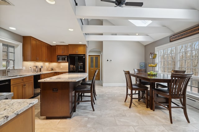 kitchen featuring light stone countertops, lofted ceiling with skylight, decorative backsplash, black appliances, and a sink