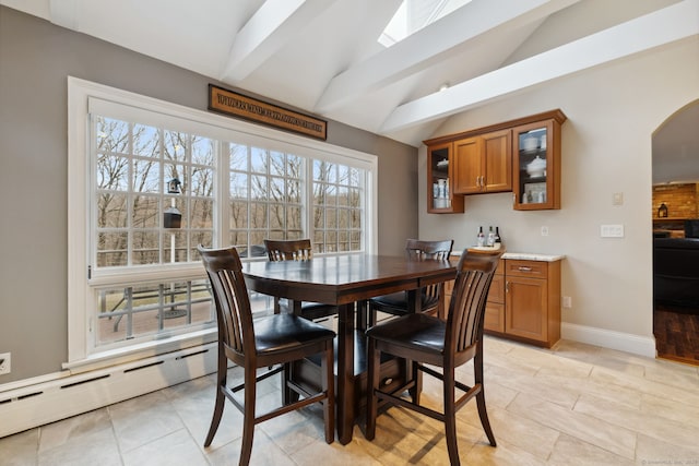 dining area with baseboards, light tile patterned floors, vaulted ceiling with skylight, arched walkways, and a baseboard radiator