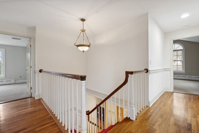 hallway featuring a baseboard heating unit, an upstairs landing, visible vents, and hardwood / wood-style floors