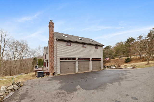 view of side of property featuring cooling unit, driveway, a chimney, and a garage