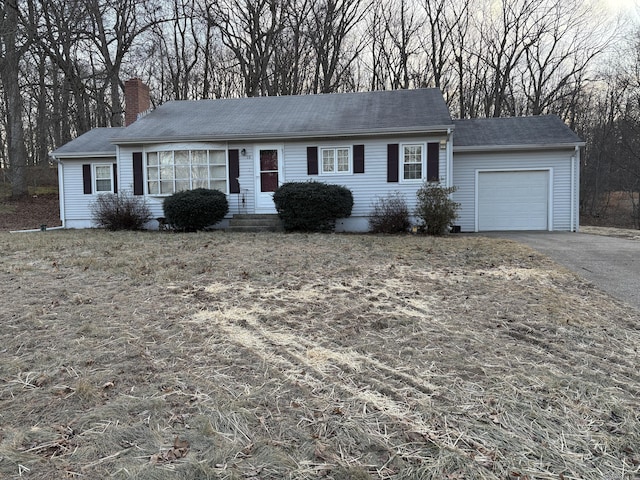 ranch-style home with a garage, a chimney, and aphalt driveway