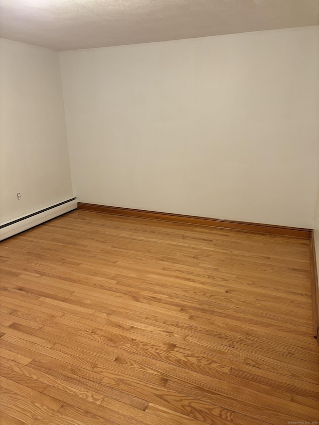 empty room featuring baseboard heating, light wood-style flooring, and baseboards