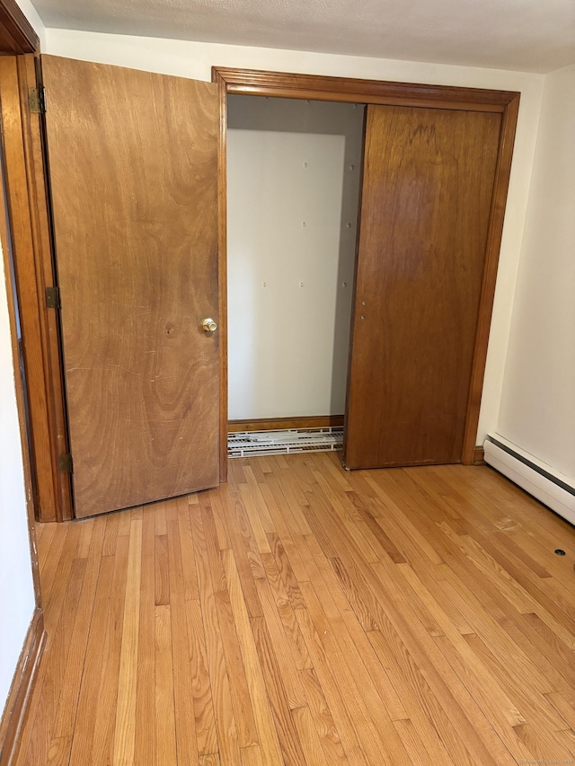 unfurnished bedroom featuring a baseboard heating unit and light hardwood / wood-style flooring