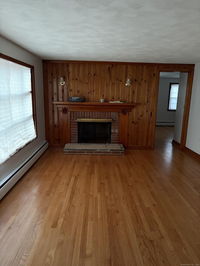 unfurnished living room featuring light wood-type flooring, baseboard heating, a fireplace, and wooden walls