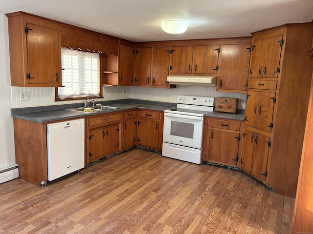 kitchen featuring white appliances, dark countertops, brown cabinets, under cabinet range hood, and a sink