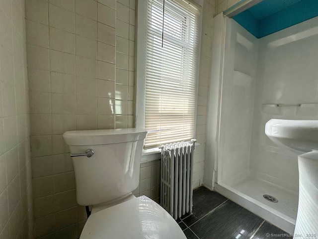 bathroom with toilet, a shower, tile patterned floors, tile walls, and radiator heating unit