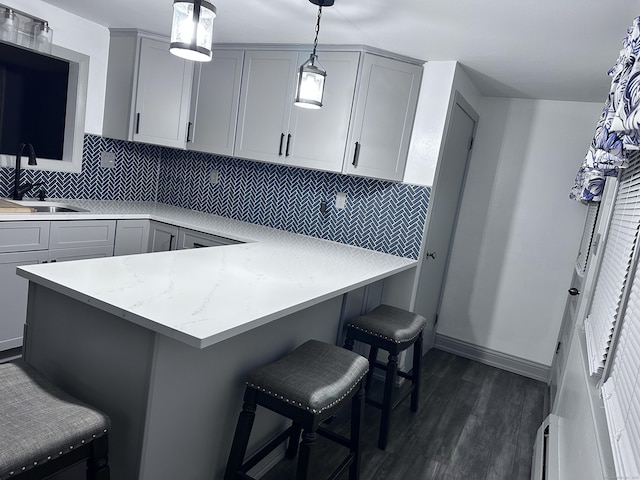 kitchen featuring a breakfast bar area, kitchen peninsula, hanging light fixtures, and gray cabinets