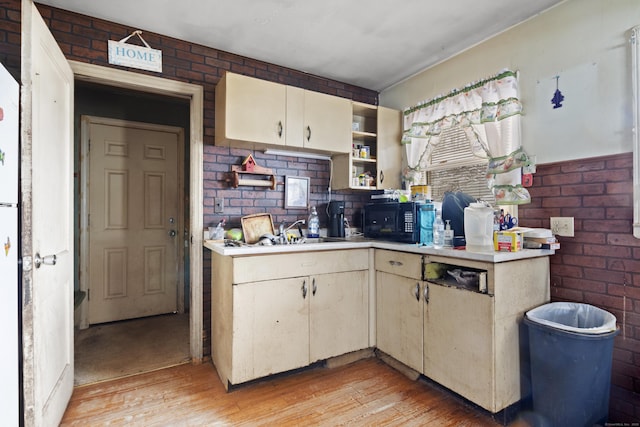 kitchen with sink, cream cabinetry, light hardwood / wood-style flooring, and brick wall