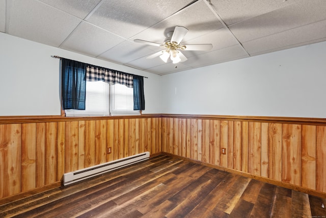 unfurnished room featuring ceiling fan, a paneled ceiling, baseboard heating, and dark hardwood / wood-style floors