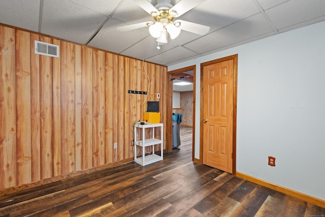 spare room with ceiling fan, a paneled ceiling, dark hardwood / wood-style flooring, and wooden walls