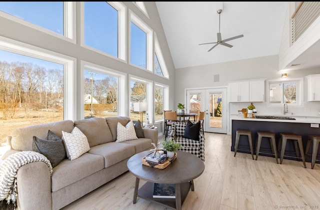 living room with high vaulted ceiling, ceiling fan, french doors, and light hardwood / wood-style floors