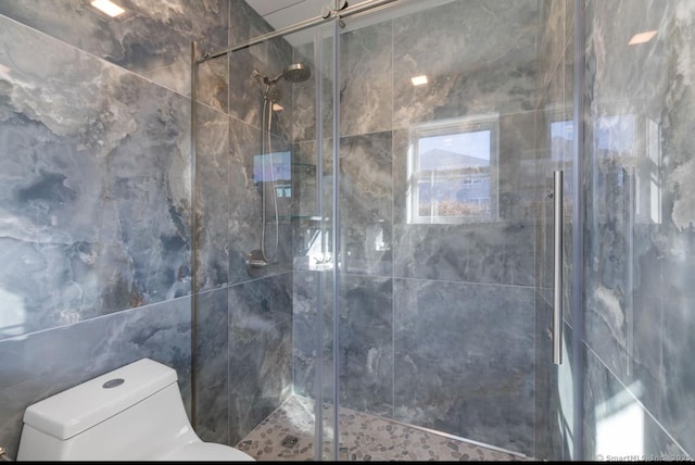 bathroom featuring toilet, tile walls, and a shower with door