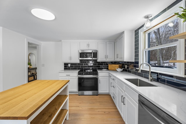 kitchen with sink, appliances with stainless steel finishes, white cabinetry, light stone counters, and decorative backsplash