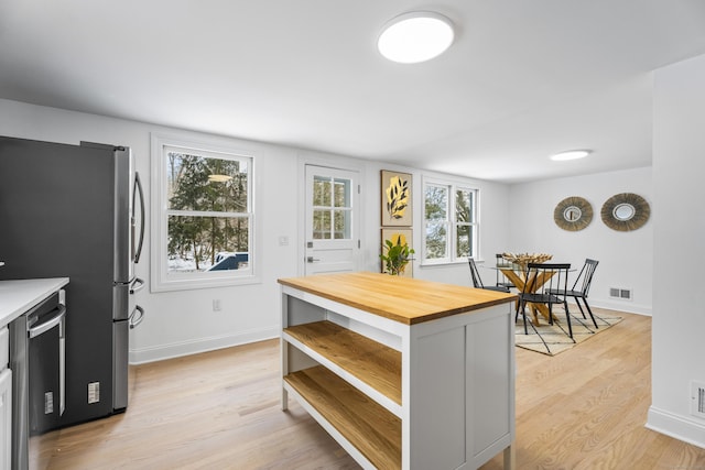 kitchen with butcher block countertops, stainless steel fridge, dishwashing machine, and light hardwood / wood-style floors