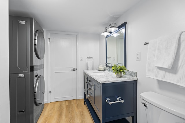 bathroom featuring stacked washer / drying machine, toilet, wood-type flooring, and vanity