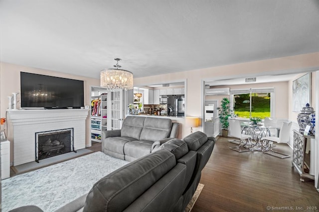 living room with dark hardwood / wood-style floors, a fireplace, a wall mounted air conditioner, and a notable chandelier