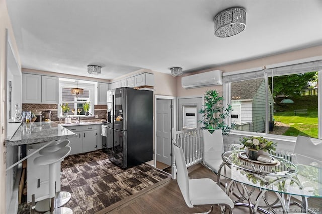 kitchen featuring light stone countertops, white cabinetry, decorative backsplash, a wall unit AC, and fridge