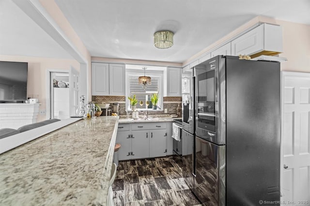 kitchen featuring decorative light fixtures, light stone countertops, decorative backsplash, and stainless steel refrigerator