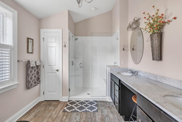 bathroom featuring lofted ceiling, wood finished floors, a sink, double vanity, and a stall shower