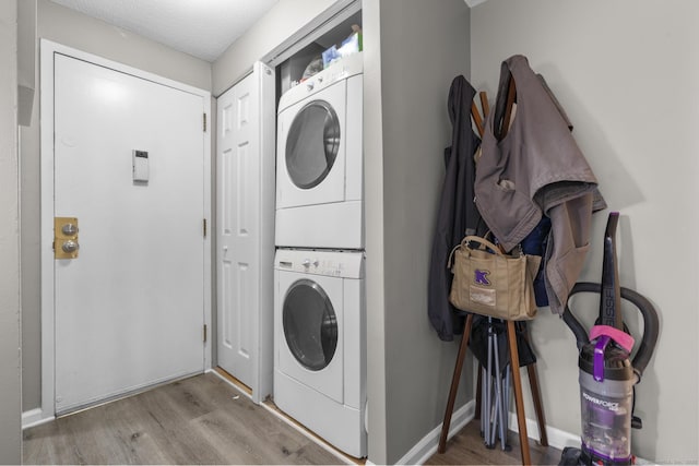 laundry room featuring light wood-type flooring, stacked washer and dryer, and a textured ceiling