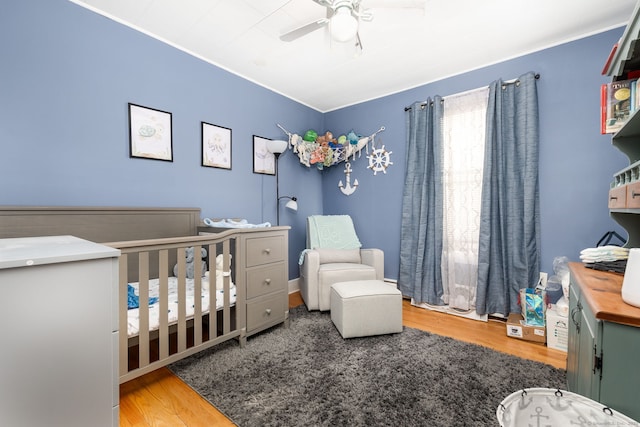 bedroom featuring ceiling fan, hardwood / wood-style flooring, and a crib