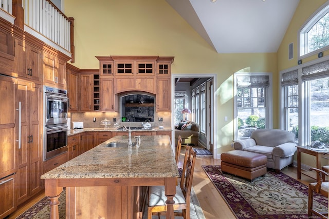 kitchen with high vaulted ceiling, an island with sink, a kitchen bar, decorative backsplash, and light stone countertops