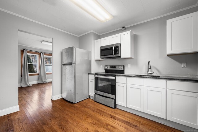 kitchen with hardwood / wood-style floors, white cabinets, appliances with stainless steel finishes, sink, and crown molding