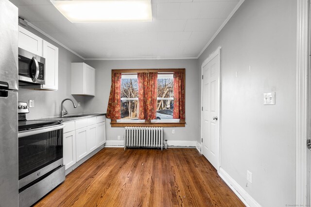 kitchen with appliances with stainless steel finishes, sink, white cabinets, and radiator heating unit