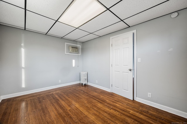 basement with hardwood / wood-style flooring, a drop ceiling, radiator, and a wall unit AC