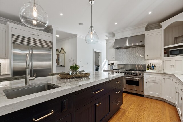 kitchen with decorative light fixtures, white cabinets, wall chimney exhaust hood, and built in appliances