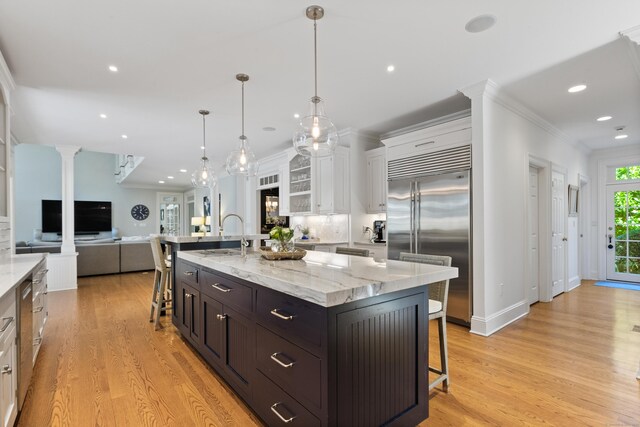 kitchen with white cabinets, stainless steel built in fridge, a kitchen breakfast bar, sink, and a large island