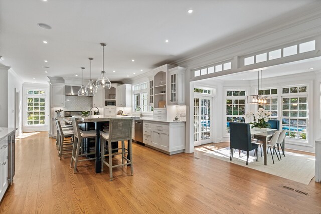 kitchen with a center island with sink, stainless steel appliances, decorative backsplash, decorative light fixtures, and light wood-type flooring