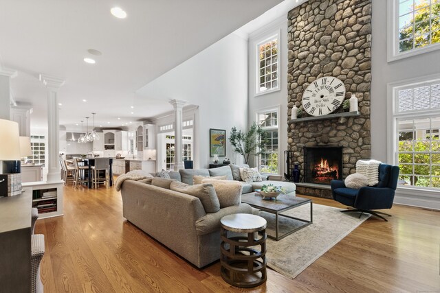 living room with a healthy amount of sunlight, a fireplace, a towering ceiling, and light hardwood / wood-style flooring