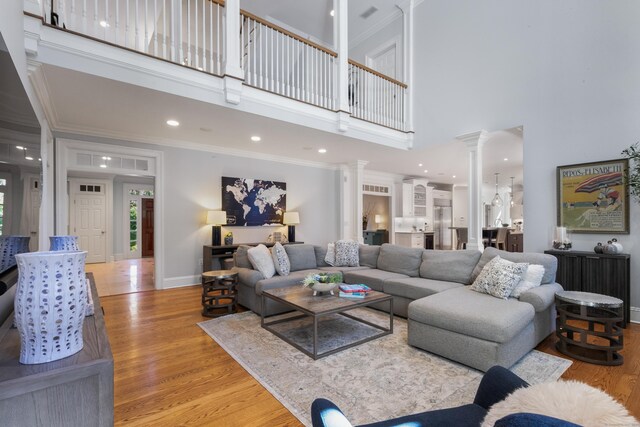 living room featuring ornamental molding, a high ceiling, ornate columns, and light hardwood / wood-style floors