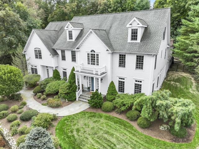 view of front of house with a shingled roof, a front yard, and a balcony